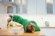 Tagesmüdigkeit Müde Frau mit dem Kopf auf dem Tisch, die den Kaffee neben die Tasse schüttet.